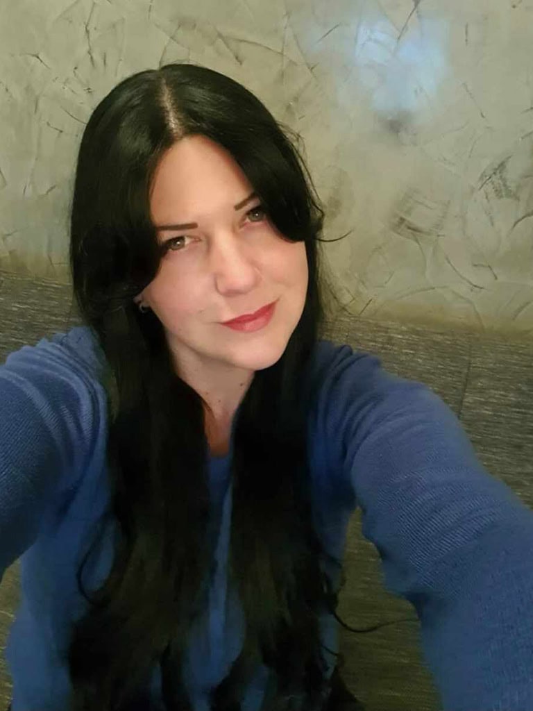 Naturkosmetik Susanne Ka: Frau mit schwarzen Haaren und blauer Kleidung, Selfie vor grauer Wand.